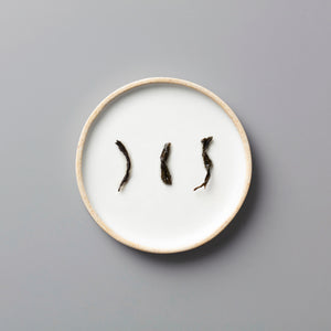Three twisted dark tea leaves of PANLAN QUE SHE yancha oolong arranged on a round white ceramic plate