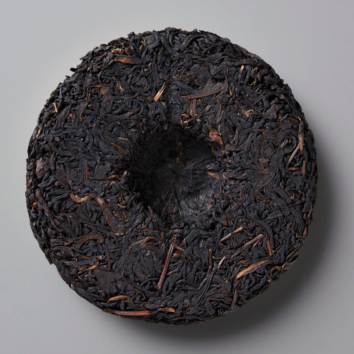 Smoke Break black tea cake, compressed dark leaves with rustic texture against grey background