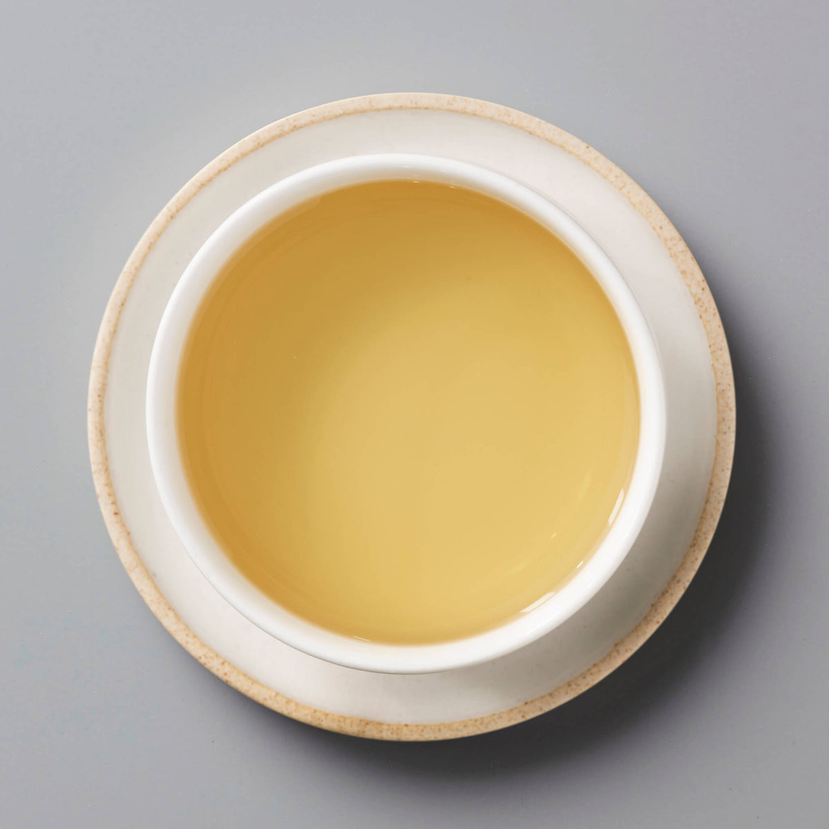 Fuding Bai Mudan white tea in a ceramic cup showing golden amber liquor against grey background