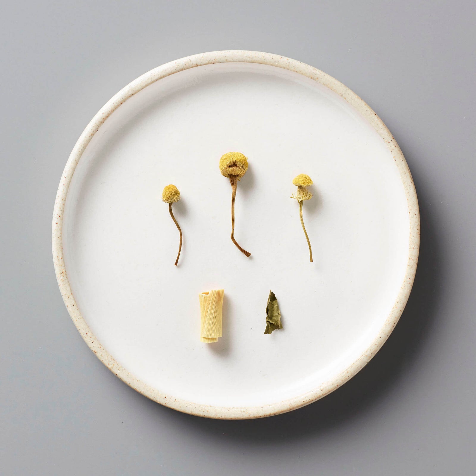 BOUQUET tisane blend ingredients on white ceramic plate: dried chamomile flowers, lemongrass, and peppermint leaf