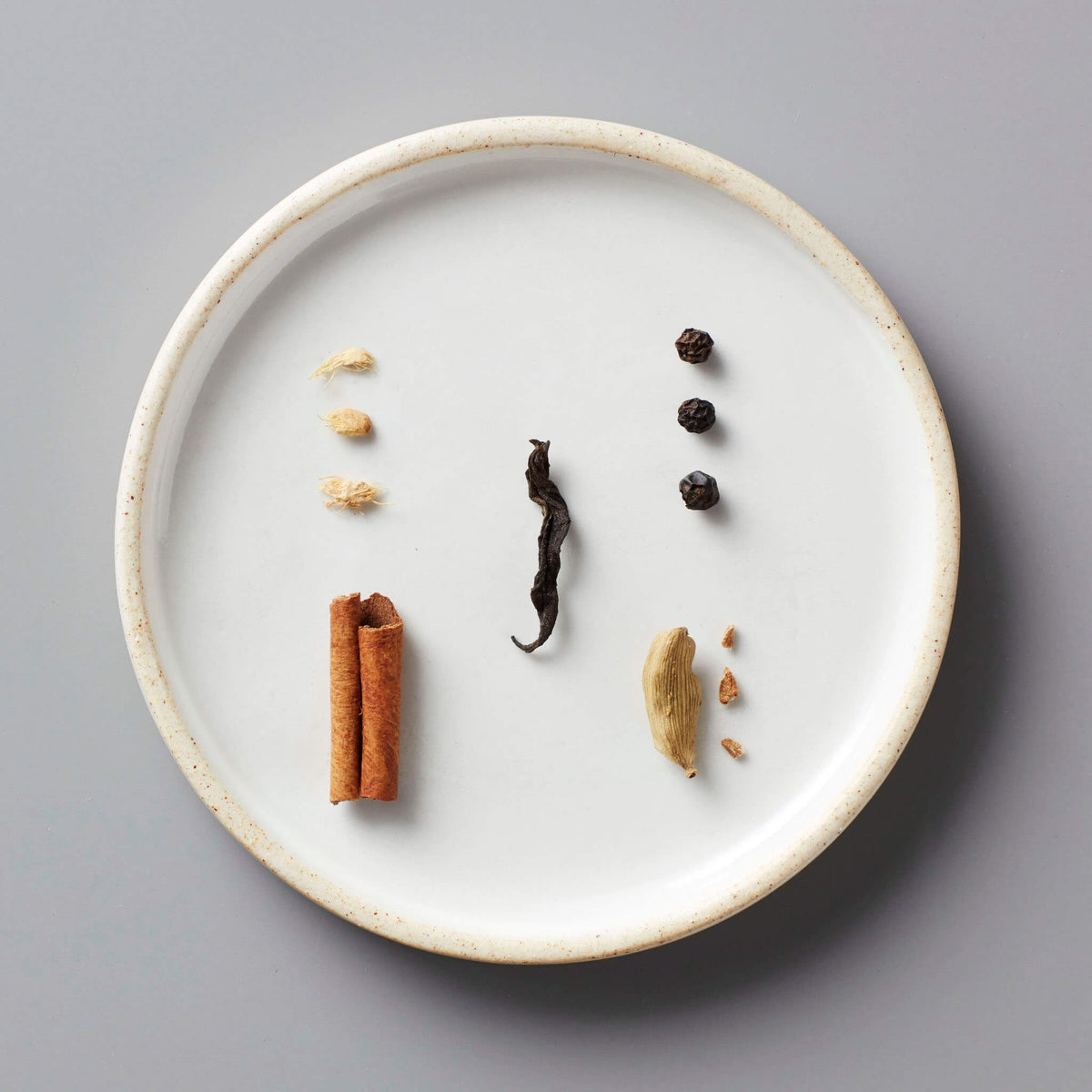Masala Chai Concentrate spices displayed on white ceramic plate including cinnamon, peppercorns, cardamom and ginger