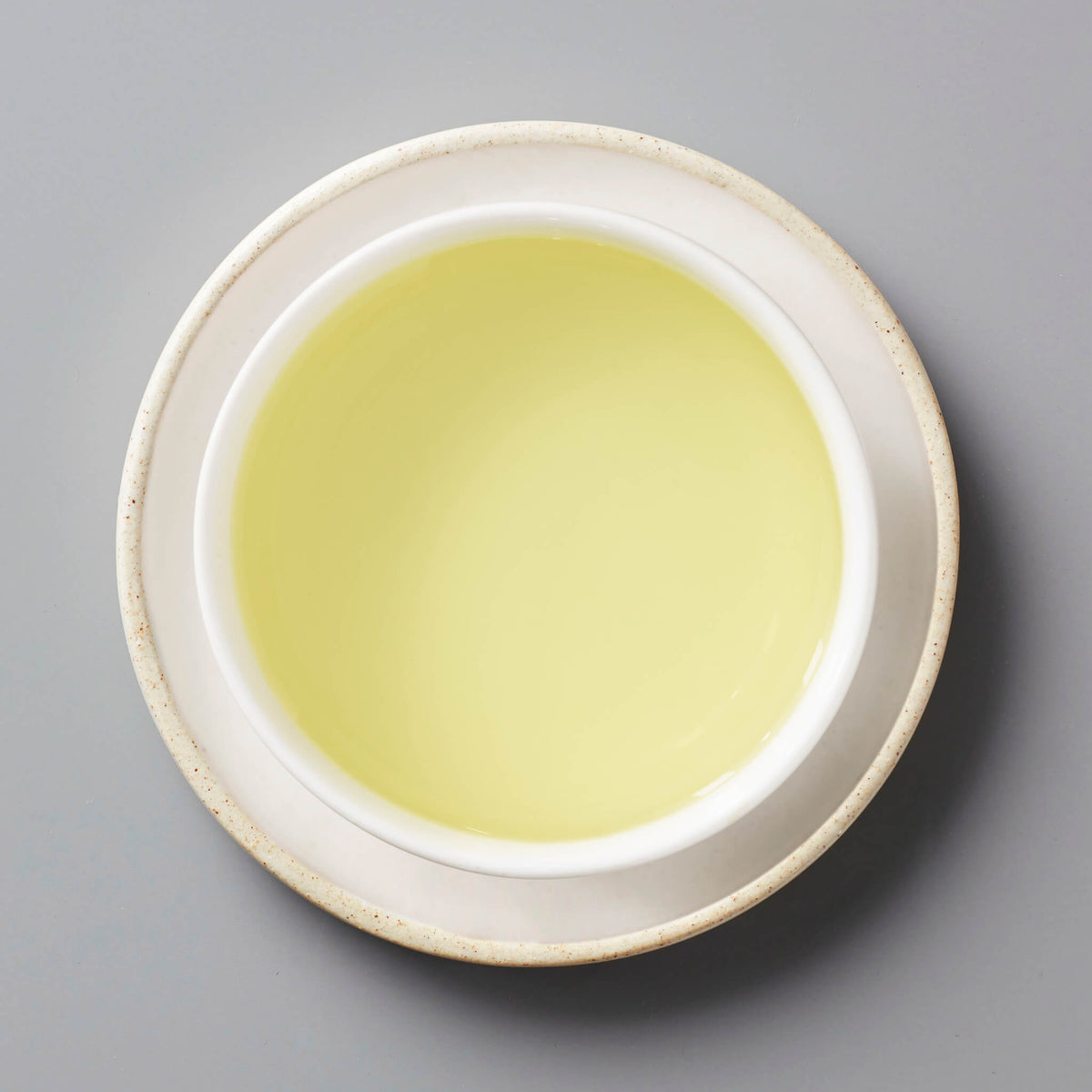 CHRYS tisane in white ceramic cup showing pale yellow chrysanthemum tea liquor against grey background