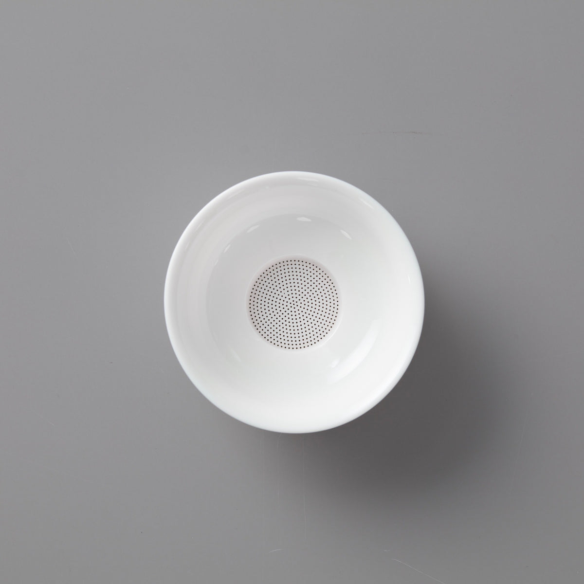White porcelain filter with perforated base featuring multiple tiny holes on elegant circular stand for tea straining