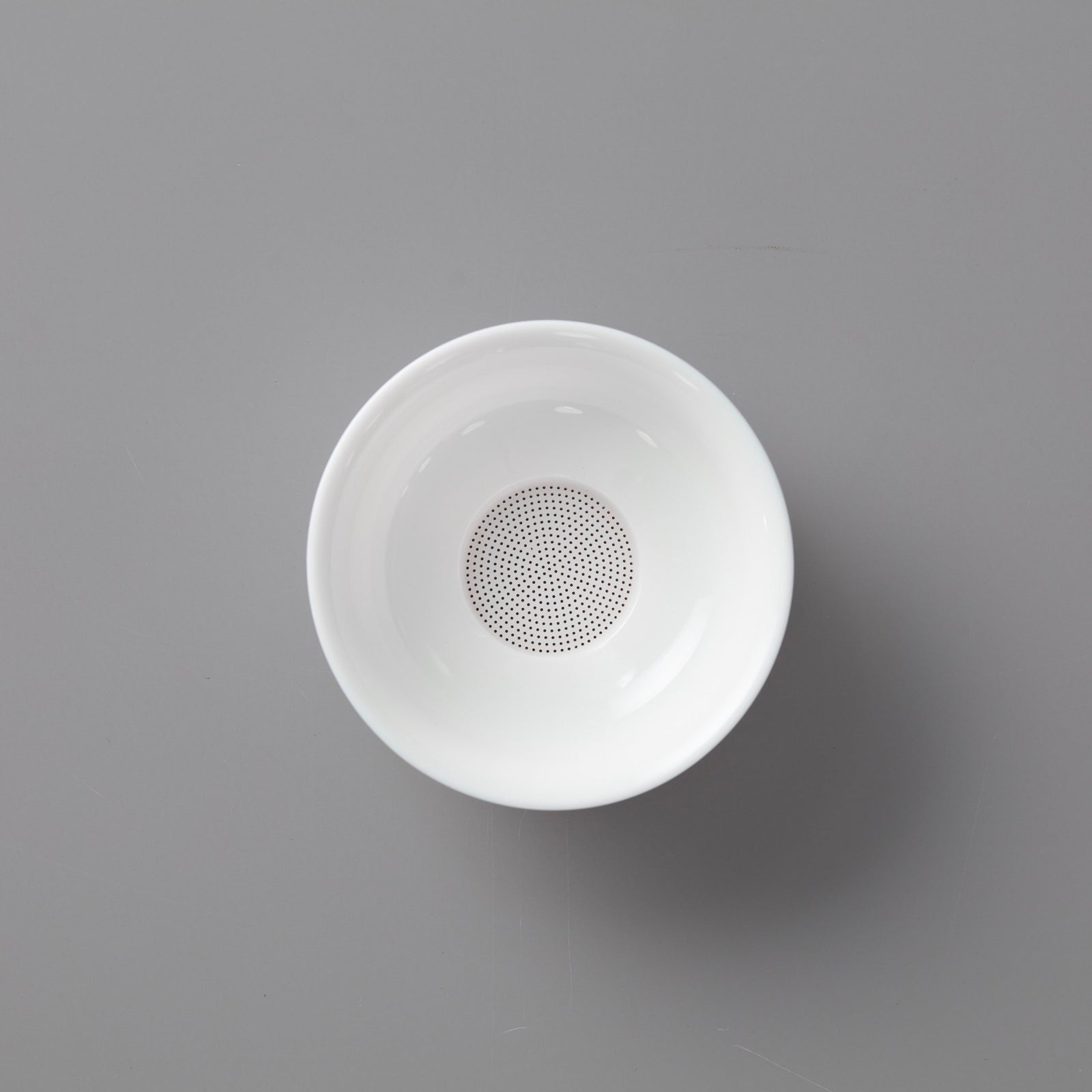 White porcelain filter with perforated base featuring multiple tiny holes on elegant circular stand for tea straining