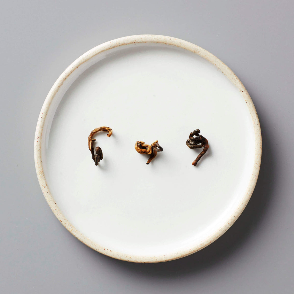 HUGO GREY black blend tea leaves artfully arranged on white ceramic plate showing natural curl and texture
