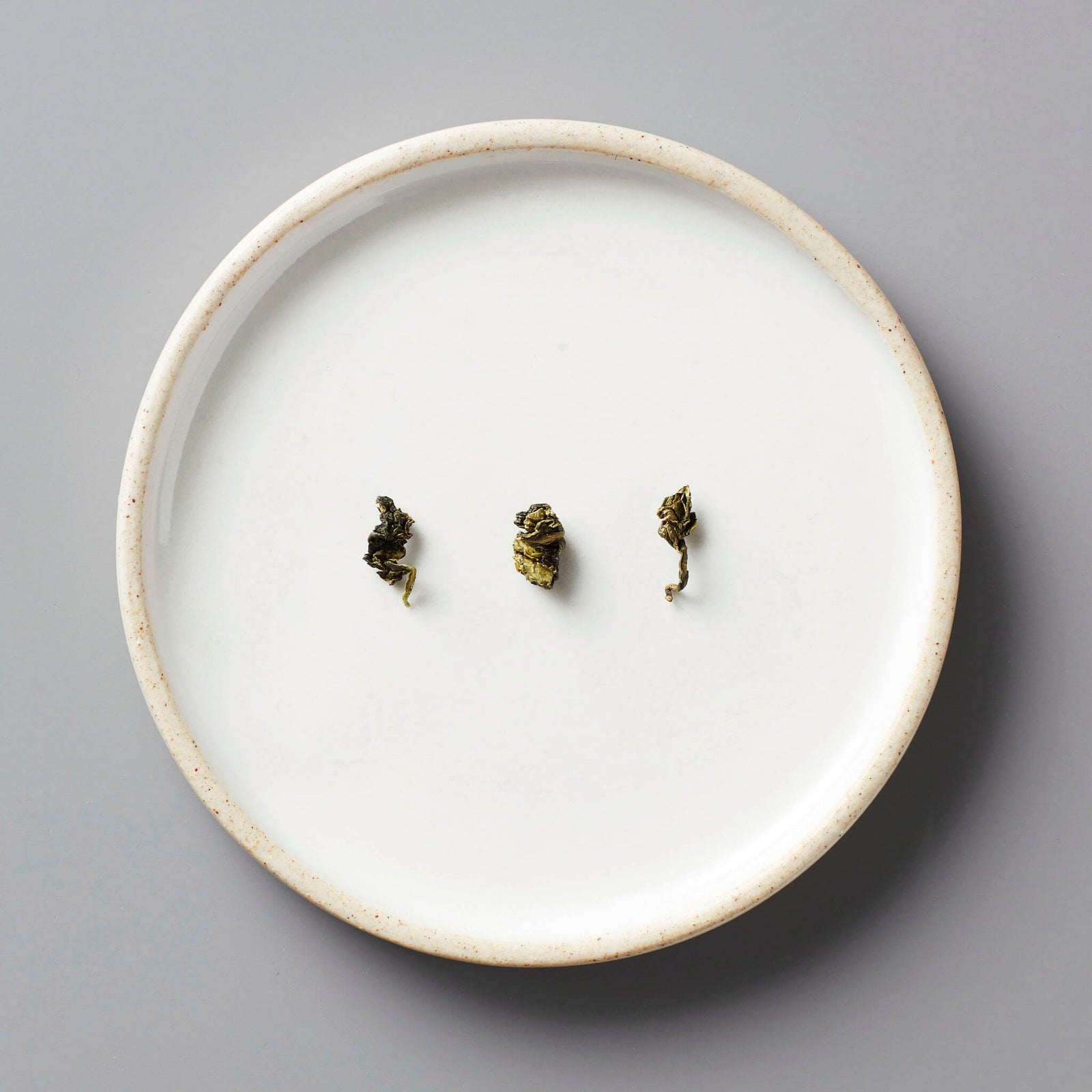 GUI SHAN oolong tea leaves arranged on a white ceramic plate, showing rolled dark green leaves against minimalist backdrop