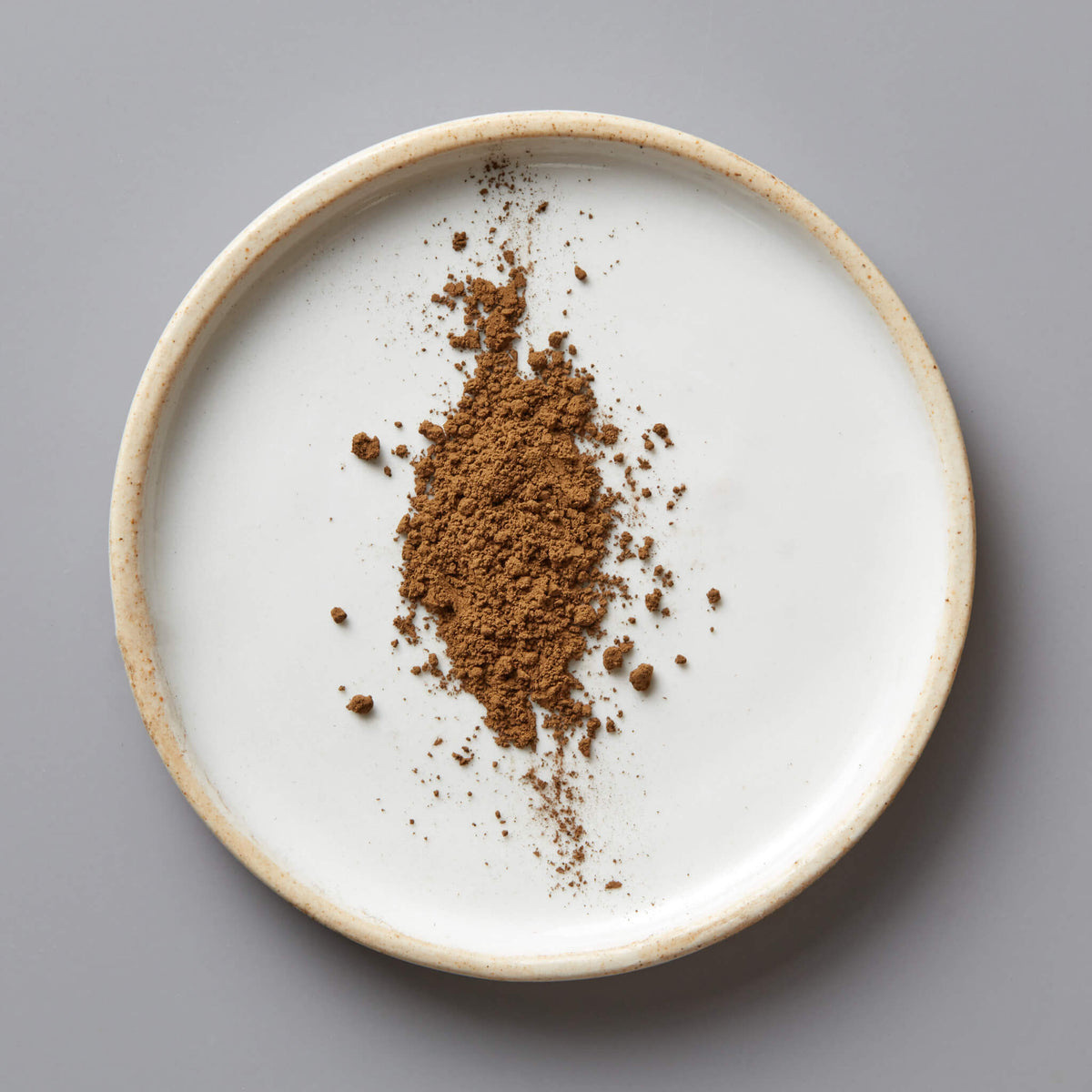 HOUJI POWDER HUGO green tea powder scattered on white ceramic plate with beige rim