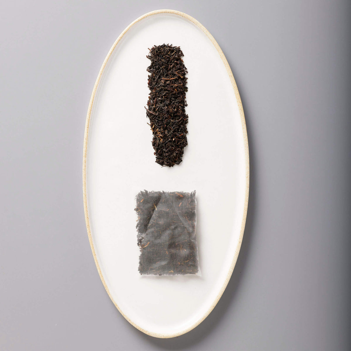 Iced Classic Black tea leaves and sachet displayed on white oval ceramic plate showing loose and packaged forms
