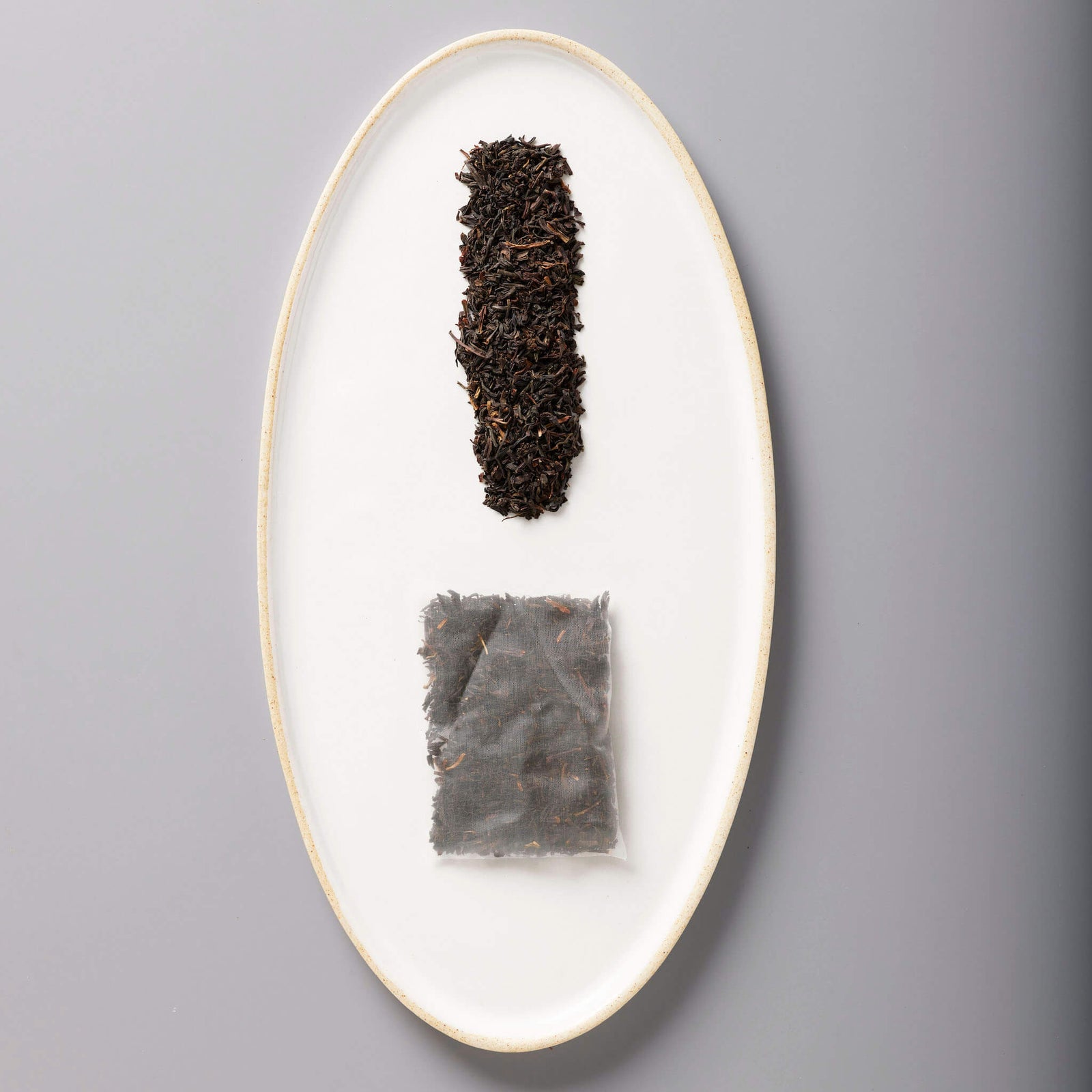 Iced Classic Black tea leaves and sachet displayed on white oval ceramic plate showing loose and packaged forms