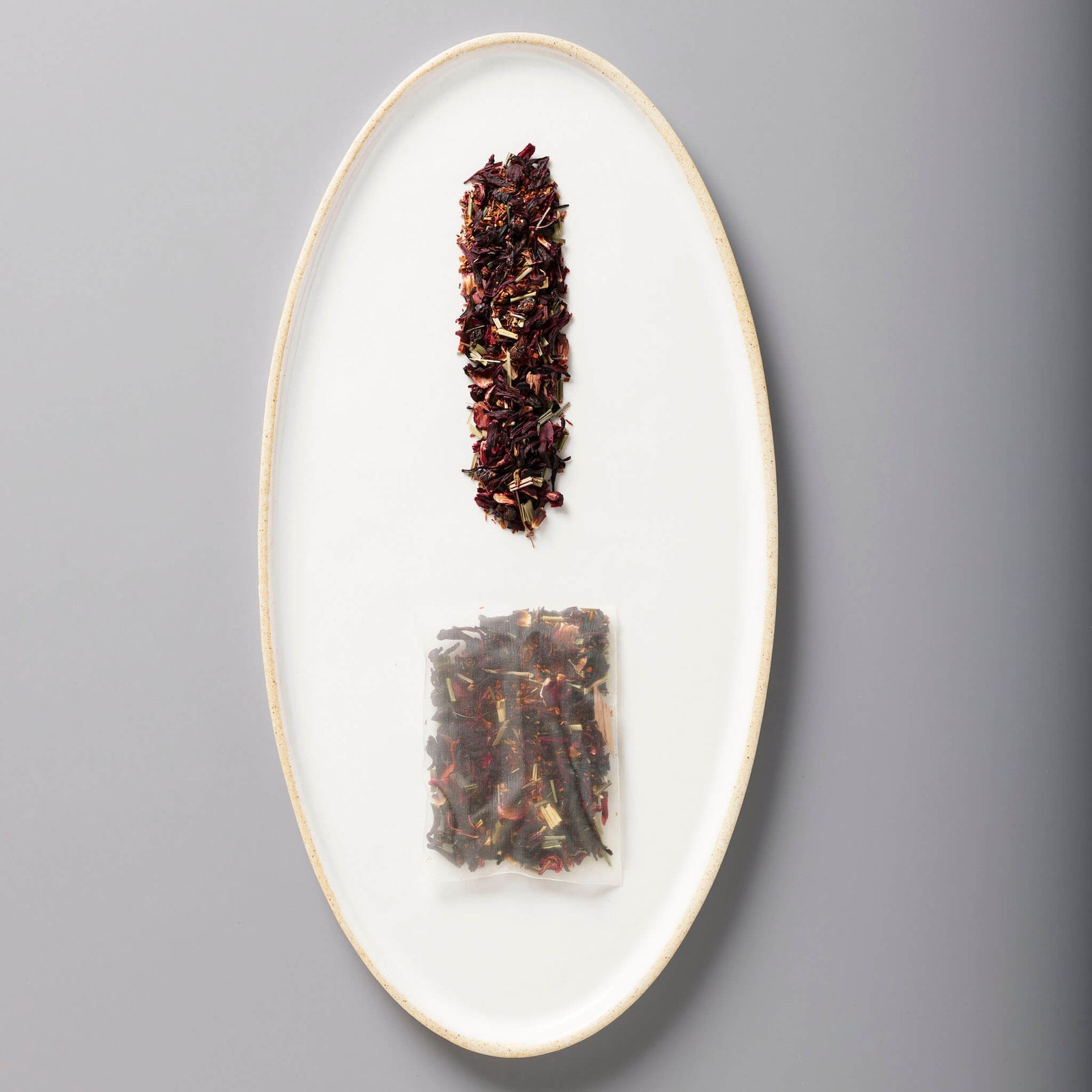 Iced Hibiscus Berry loose leaf blend and tea bag on white oval plate showing deep purple-red organic tisane mix