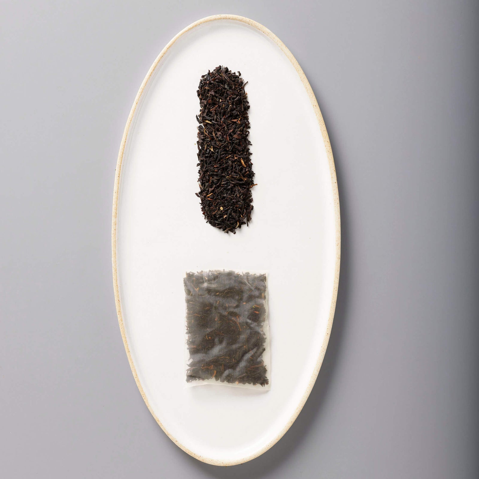 Iced Mango Black tea leaves and sachet on white oval plate showing loose and packaged tea forms