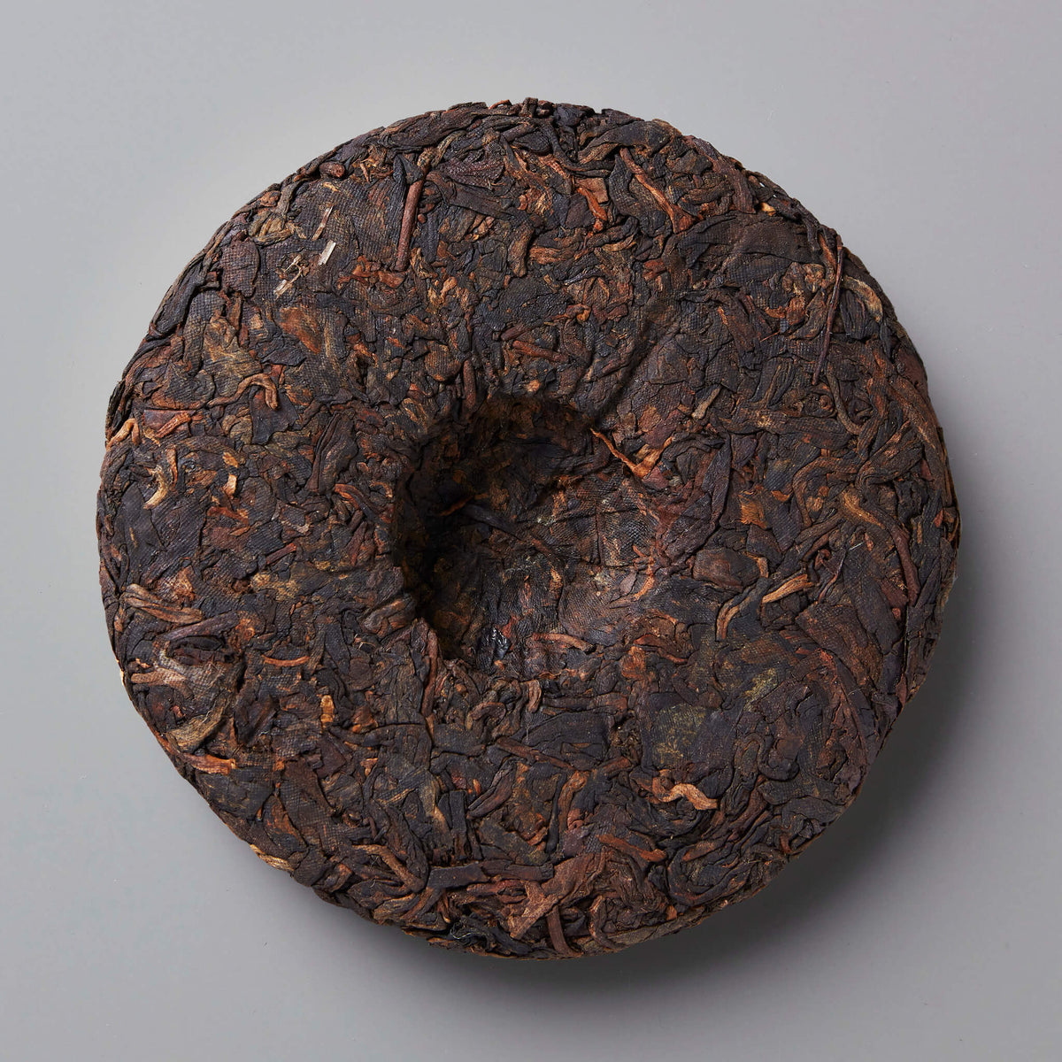 Ink Jet shou puer tea cake showing dark compressed leaves with rustic texture and center depression on grey background