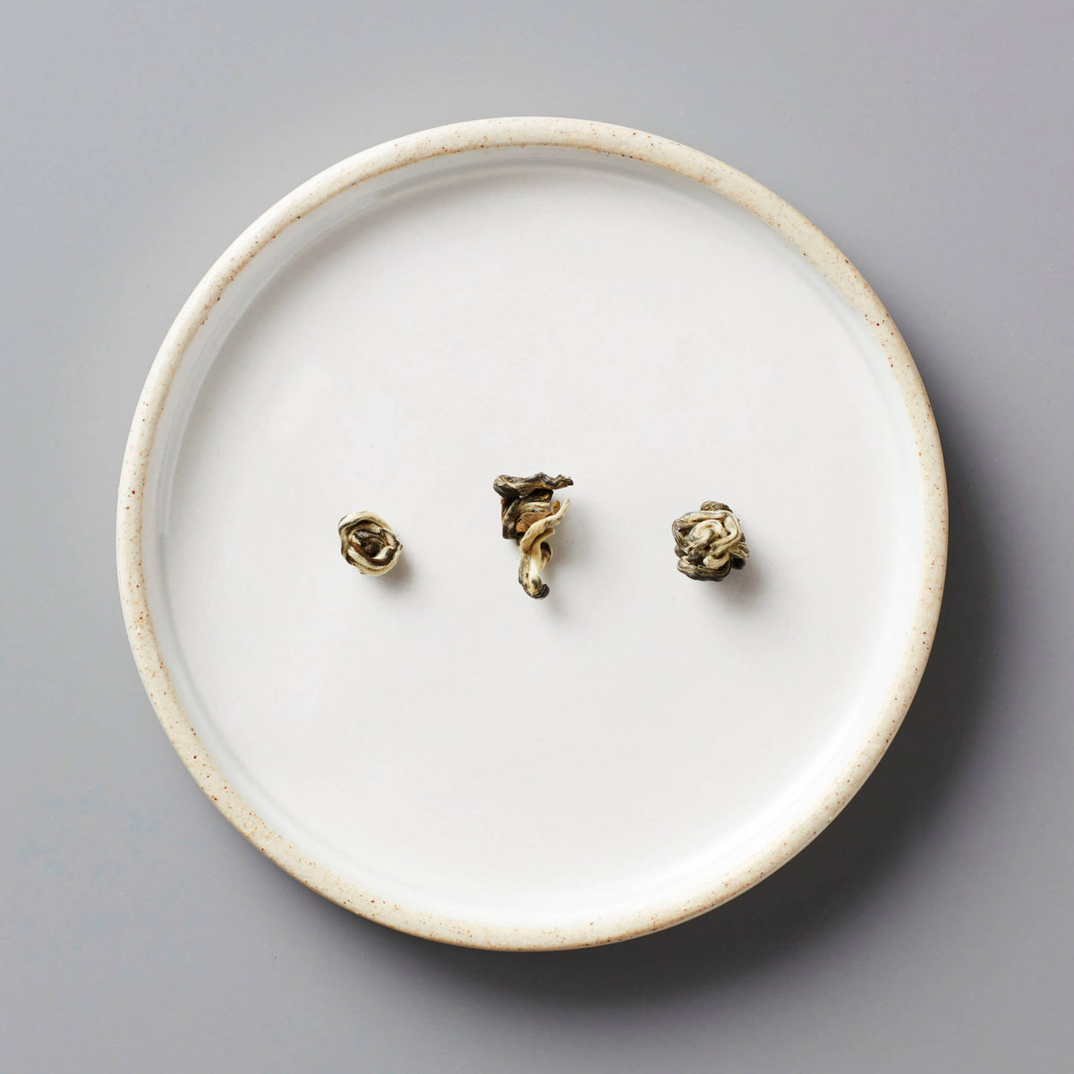Jasmine Bai Hao scented green tea pearls on white ceramic plate showing delicate rolled leaves for steeping
