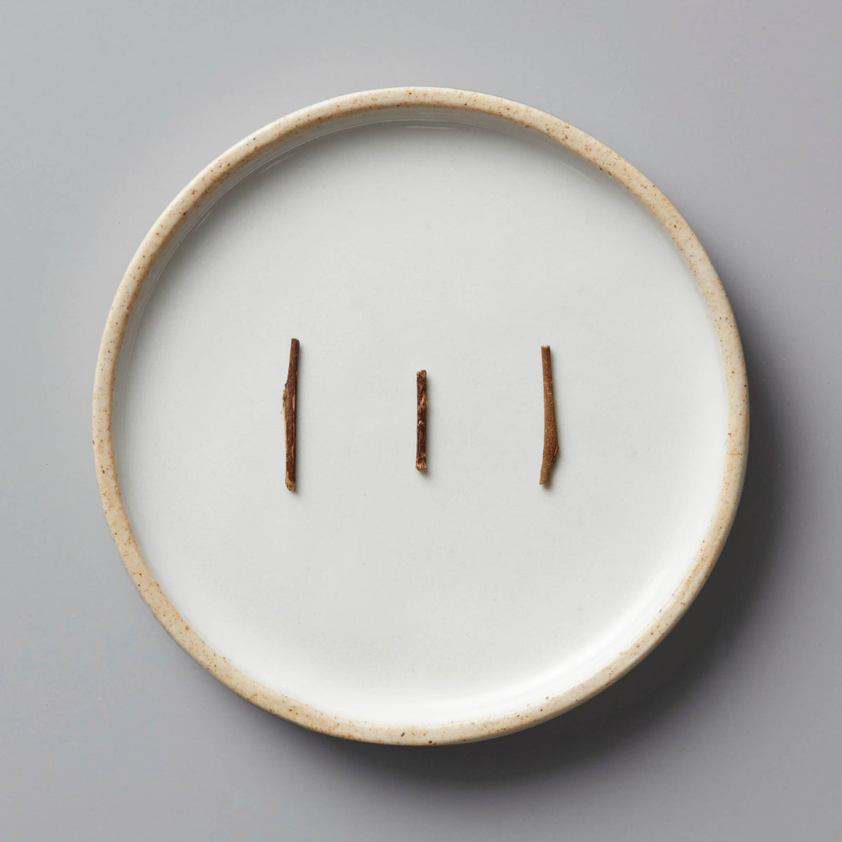 Kabuse Houjicha green tea stems on white ceramic plate with beige rim showing natural roasted color and texture