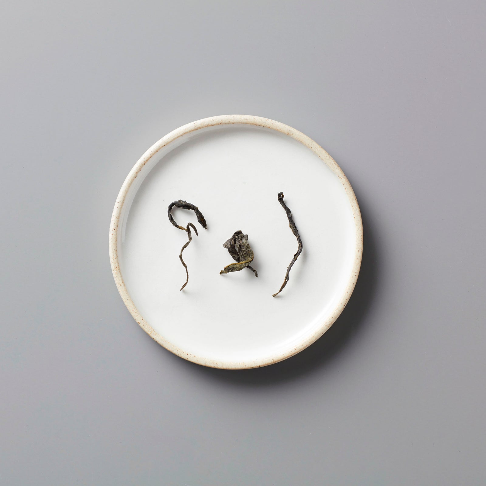 Long Kou Maofeng green tea leaves displayed on white ceramic plate showing delicate twisted dry leaf form