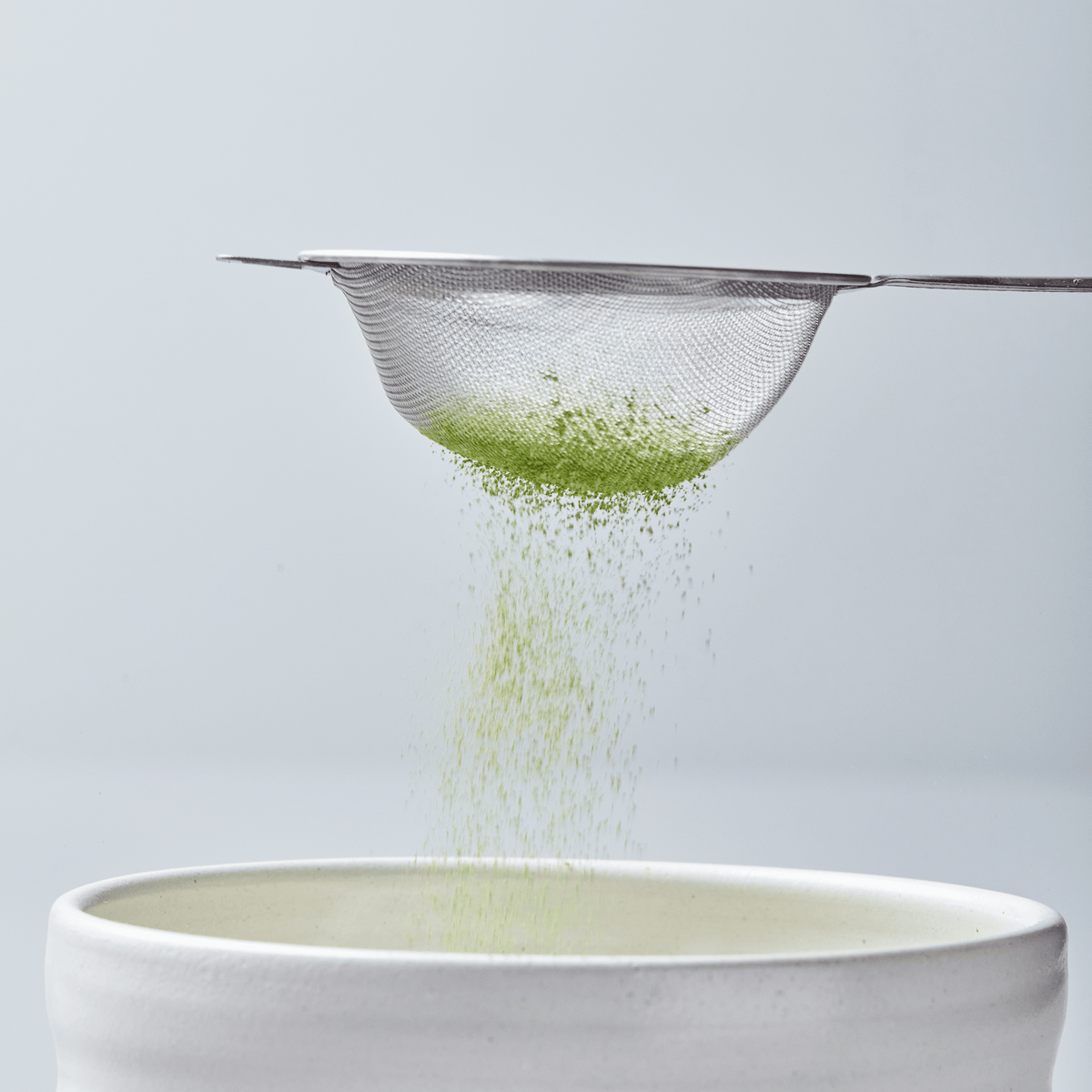 Matcha Sifter sieving bright green tea powder into white ceramic bowl against light gray background