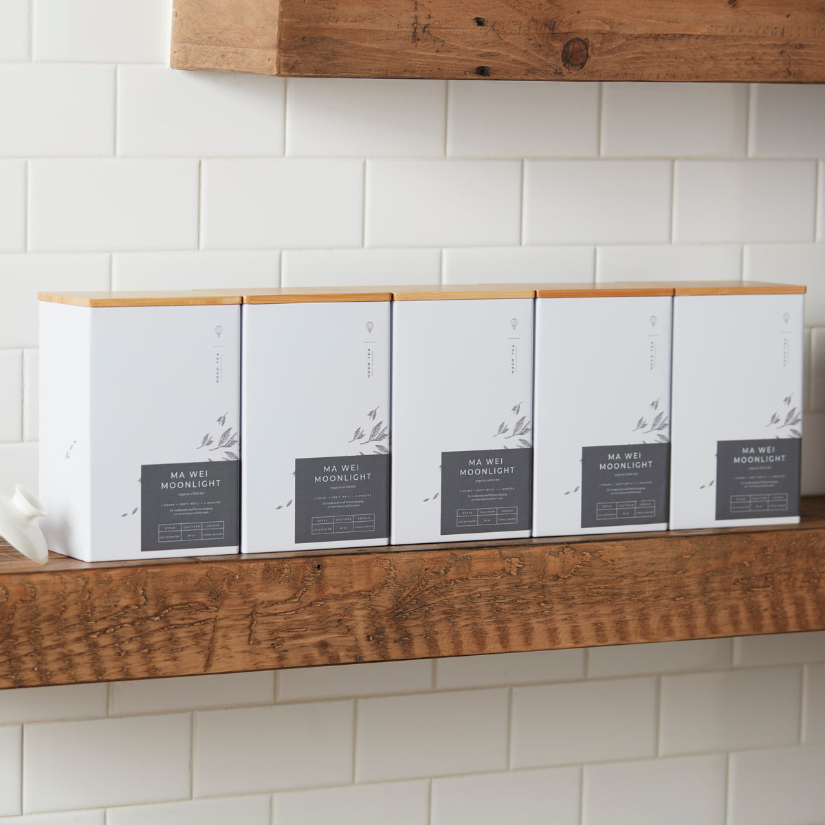 Storage Can MIYABI white tea tins with bamboo lids arranged on wooden shelf against white tile wall